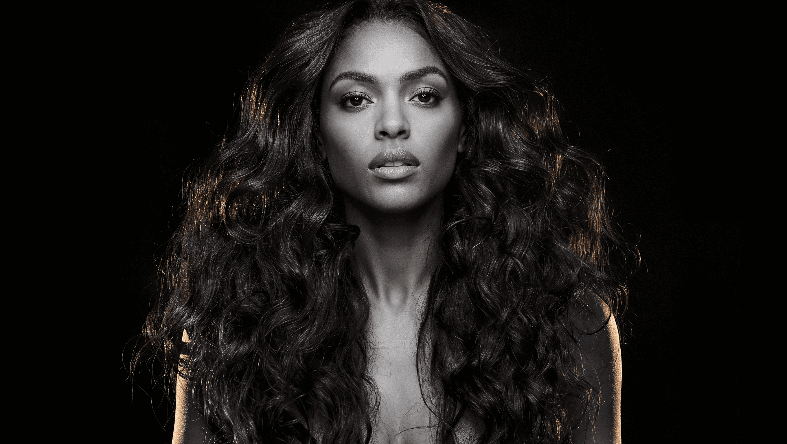 Wig Man model wearing a voluminous curly human hair wig, black and white editorial with subtle gold rim light